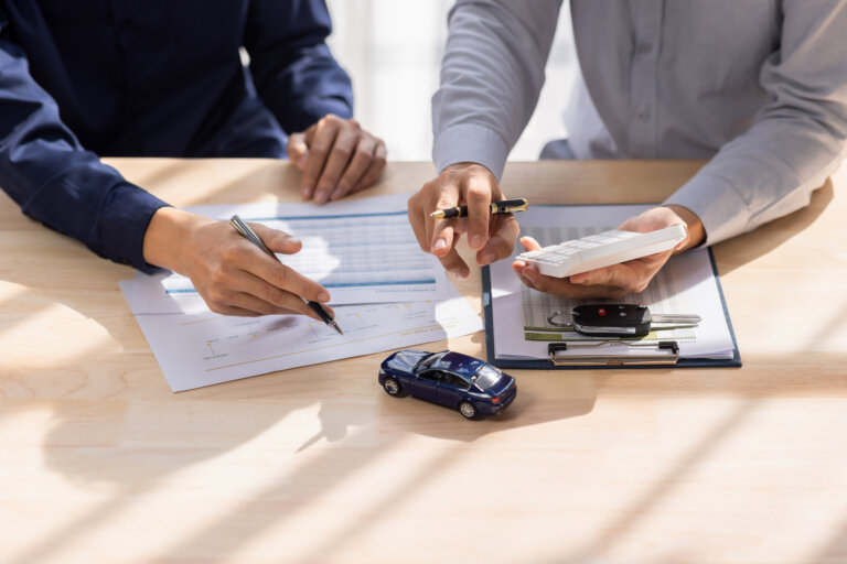Alt-text suggestion: **Two people reviewing car finance paperwork with keys and a calculator on the table**
