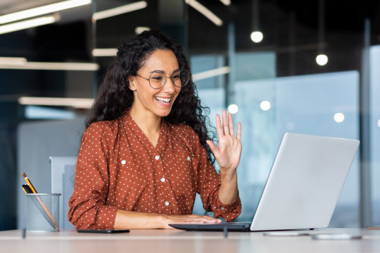 Woman smiling and waving while on a video call with laptop