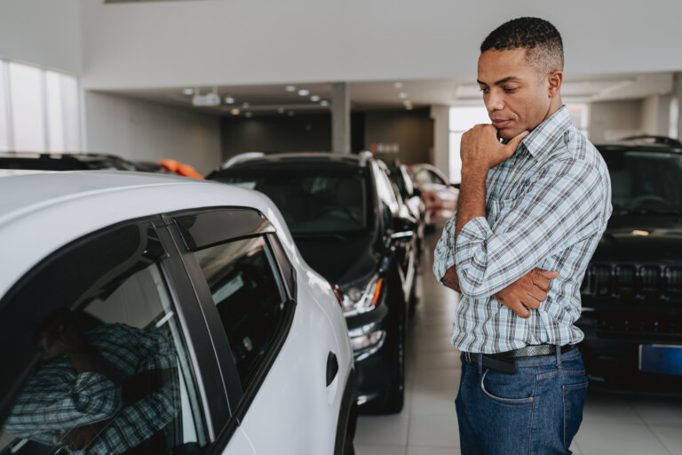 Man in a car dealership thoughtfully examining a white vehicle