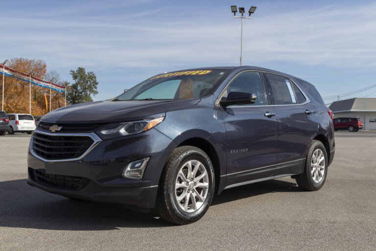 A dark gray Chevrolet Equinox is parked in a car dealership lot on a sunny day.