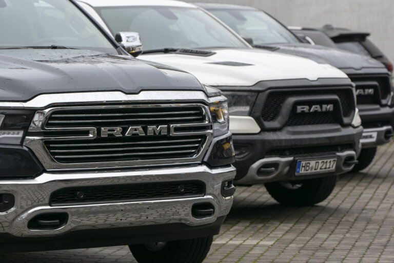 A line of new Ram pickup trucks is parked, with a close-up on the grilles of the first two vehicles.