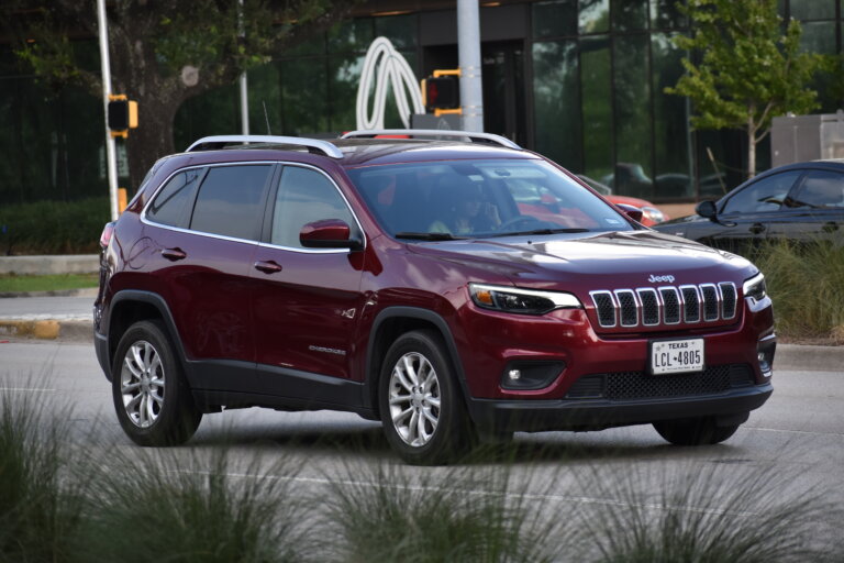 A red Jeep SUV is driving on a city street.