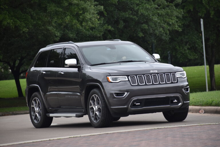 Gray Jeep SUV parked on a street with trees in the background.