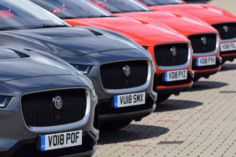 A close-up of the front of several Jaguar E-Pace SUVs parked in a row. The vehicles are in different colors, including red and gray.
