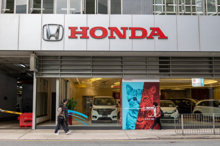 Pedestrians walk past a Honda dealership in the Philippines, showcasing new cars and a vibrant ad.