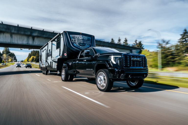 Black GMC truck towing a large Road Warrior trailer on highway.
