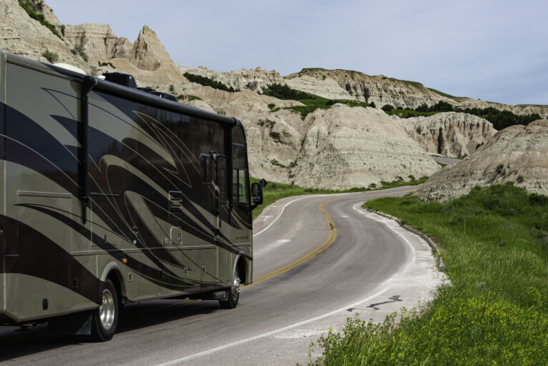 RV driving on a winding road through rocky hills and green grass.
