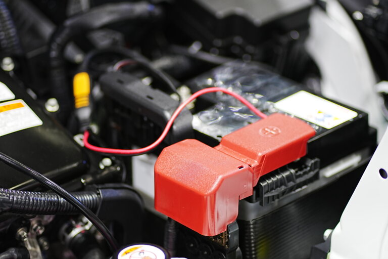 Close-up of a car battery with red positive terminal cover and connected cables