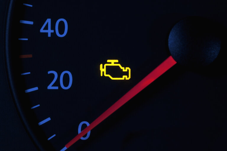 Car dashboard with illuminated yellow check engine warning light.