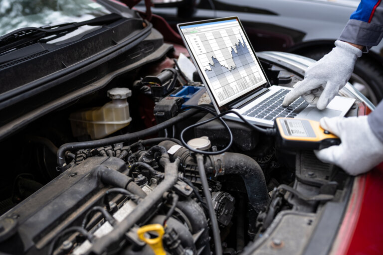 Mechanic using laptop and diagnostic tool to check car engine performance.