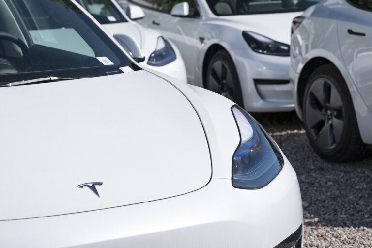 A close-up of a white Tesla Model 3, with many identical cars parked behind it.