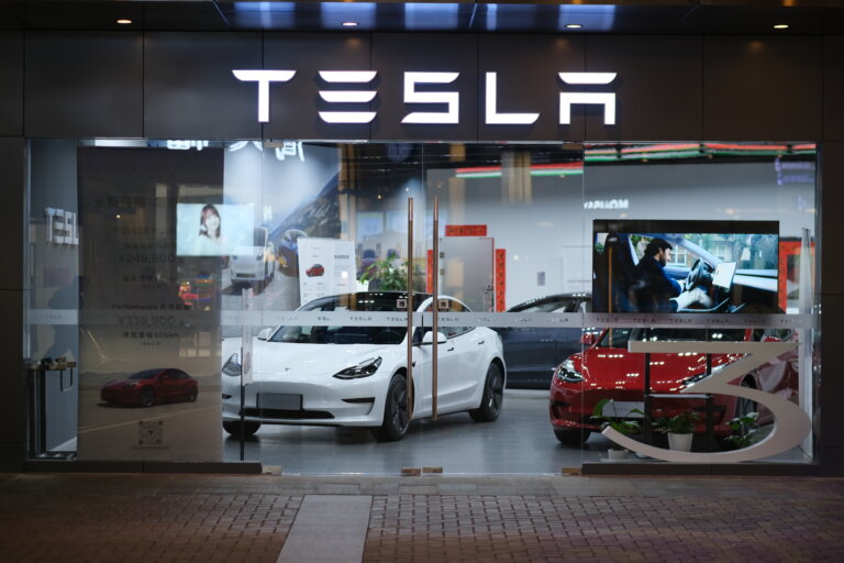 The brightly lit storefront of a Tesla showroom at night, with several cars on display.