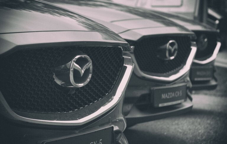 A grayscale close-up shows the front grilles and logos of a row of Mazda CX-5 SUVs.