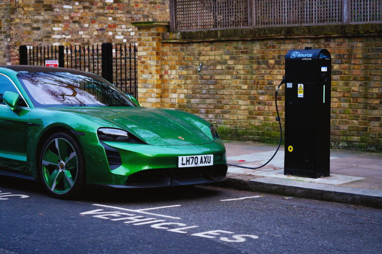 A bright green Porsche Taycan is parked and charging at an electric vehicle charging station on a city street.