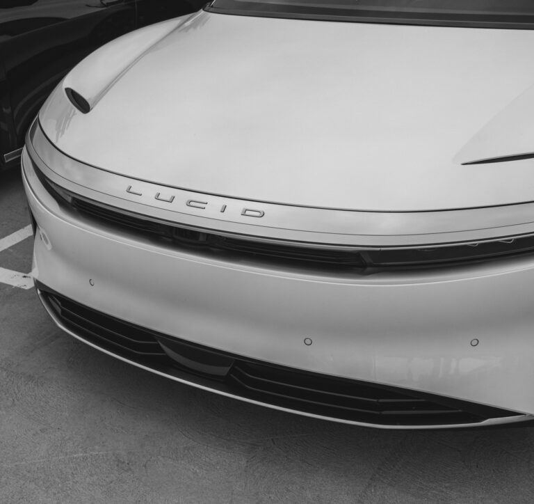 Close-up of the front of a Lucid Air sedan, showing the Lucid emblem, grille, and bumper.