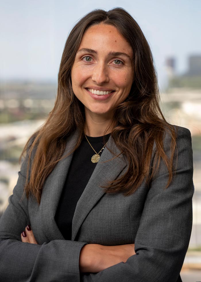 Anika smiling with her arms crossed, wearing a gray blazer against a softly blurred background.