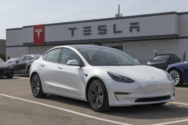 A white Tesla Model 3 car is parked in front of a Tesla dealership.