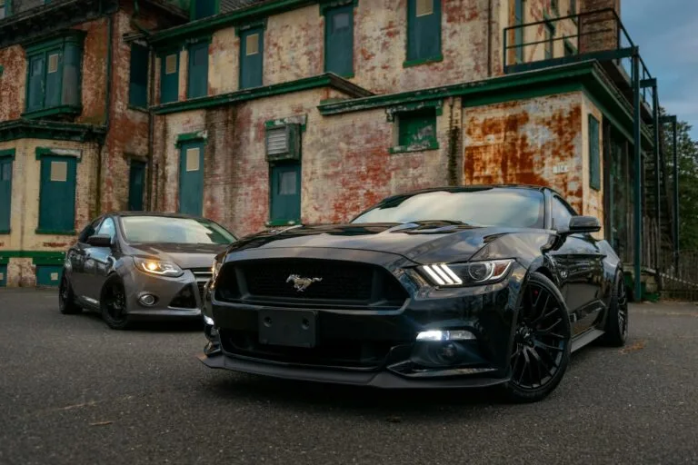 Black and gray Ford Mustang cars parked outside a weathered building, with the black car in the foreground.